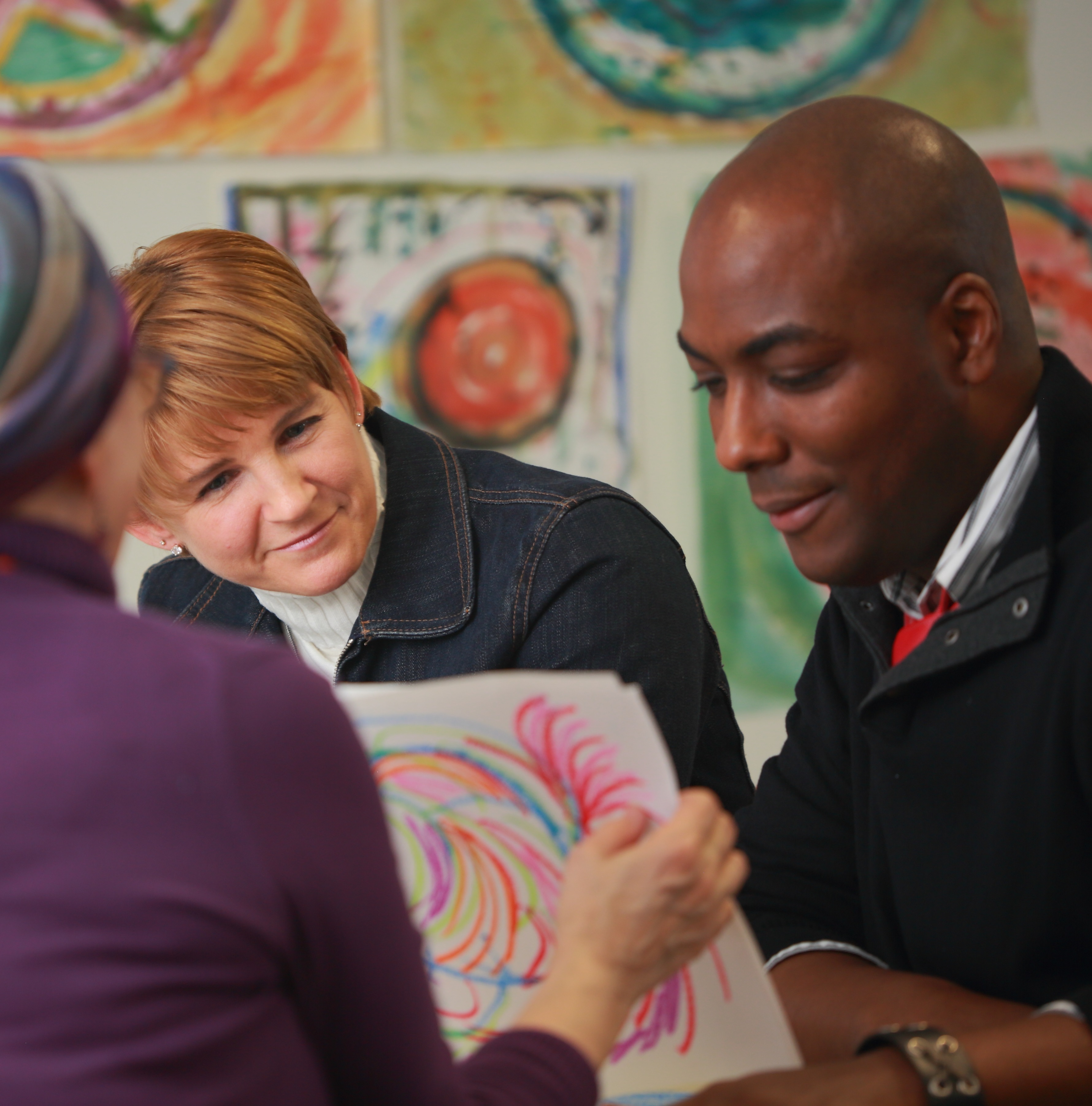 Two white women and one Black male sitting around a table looking at a piece of art.